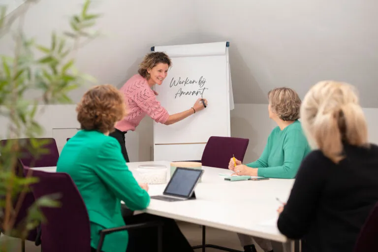 Amarant als werkgever, vier communicatiemedewerkers zijn in een vergadering, drie medewerkers zitten aan tafel. Een medewerker schrijft op een presentatiebord