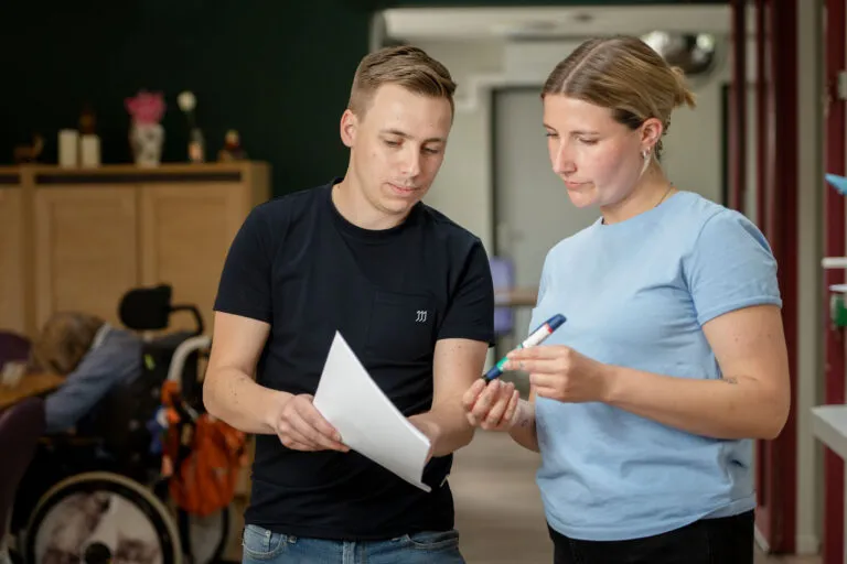 Amarant als werkgever, twee zorgmedewerkers praten met elkaar, een van de twee laat papieren zien aan de ander