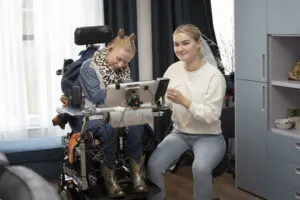 Doelgroep NAH, cliënt zit in rolstoel met tablet, begeleider ondersteunt bij een taak en kijkt