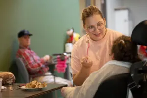 Doelgroep EVB complex. Cliënt zit in rolstoel en krijgt eten. Zorgmedewerker voert cliënt met lepel