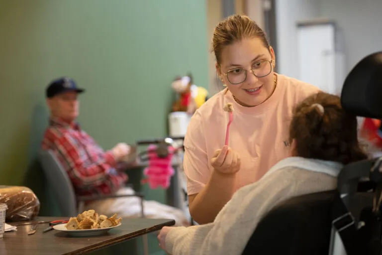 Doelgroep EVB complex. Cliënt zit in rolstoel en krijgt eten. Zorgmedewerker voert cliënt met lepel